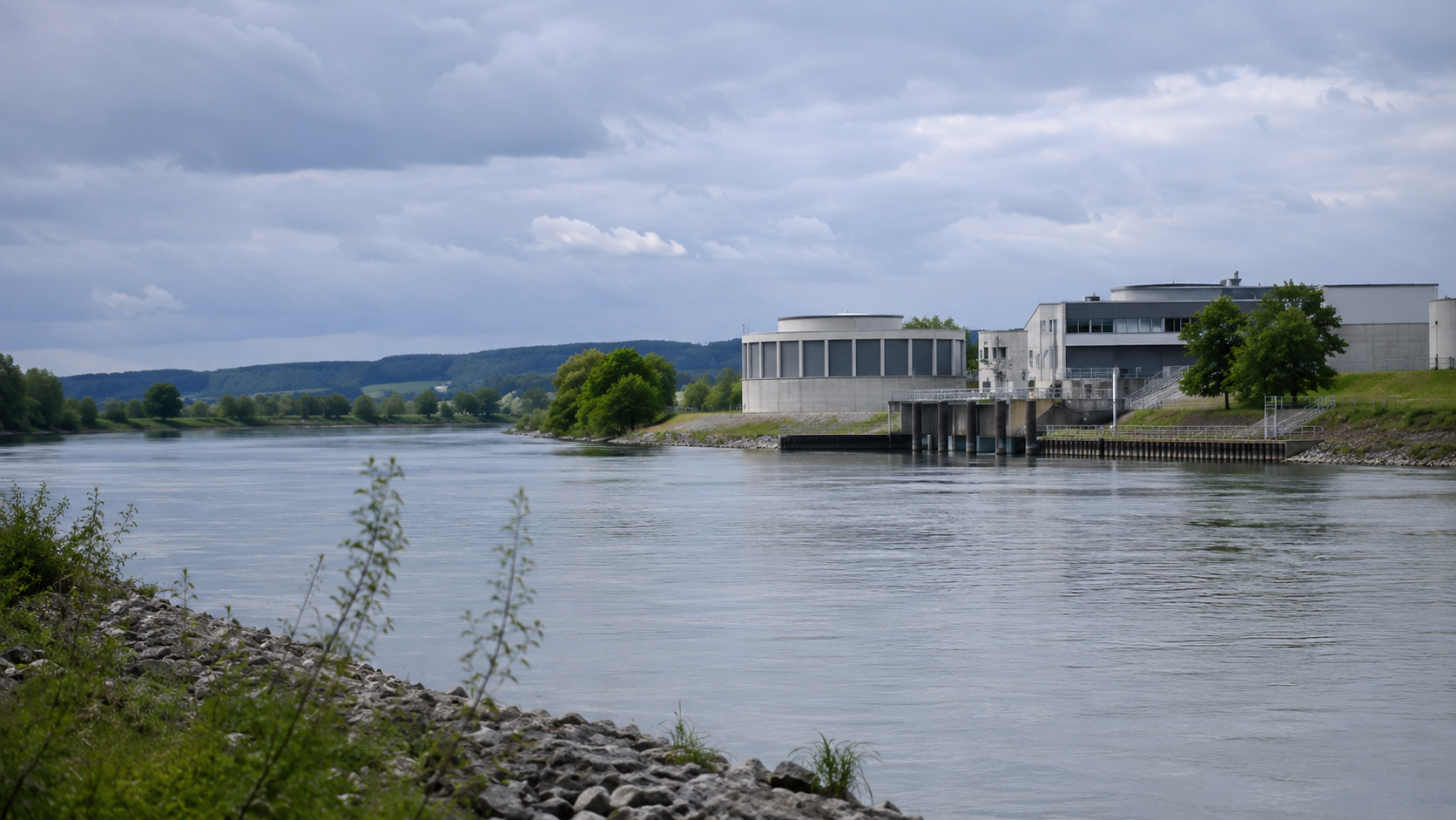 Symbolbild eines modernen Wasserwerks an einem Fluss unter bewölktem Himmel.
