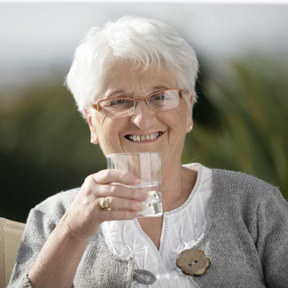 Früher war gutes Mineralwasser günstiger. Ältere Frau trinkt zufrieden frisches gereinigtes Wasser aus einem Glas